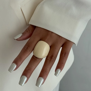 Close-up of wide cream resin ring on hand with elegant white suit and silver nails