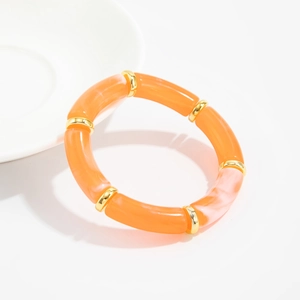 Detail of orange resin bamboo style bracelet with golden metal rings on white ceramic