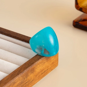 Detail of a wide light blue resin ring with gradient effect on a wooden jewelry stand