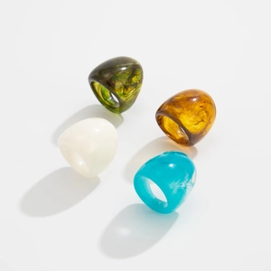 Close-up of four chunky acrylic resin rings in green, amber, white and blue colors