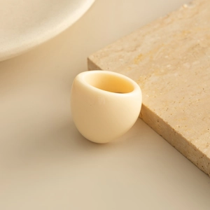 Minimalist creamy beige resin wide ring resting on a textured travertine stone base