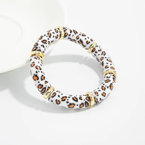 Detail of leopard print acrylic tube bracelet with golden spacers on a white ceramic plate