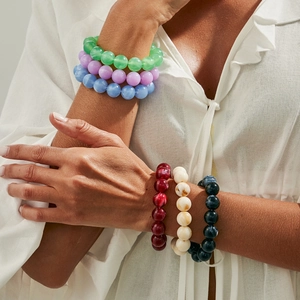 Nahaufnahme bunter Acryl-Perlenarmbänder in Grün, Lila und Blau am Handgelenk eines Models