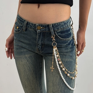 Dettaglio catena in vita a strati con strass, perle e pendente a croce su denim