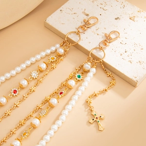 Dettaglio di un ciondolo per borsa dorato con perle, fiori di cristallo e croce pendente
