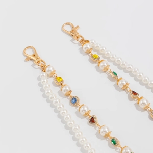Dettaglio catena per pantaloni con perle bianche e ciondoli a fiori con gemme colorate