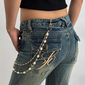 Dettaglio catena per pantaloni dorata con perle e gemme verdi su jeans vintage