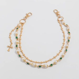 Dettaglio di una catena dorata con perle, gemme verdi e un pendente a croce colorato