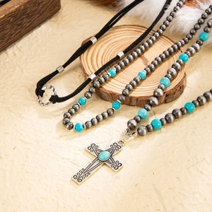 Close-up of bohemian turquoise cross pendant with silver beads on a textured wood surface