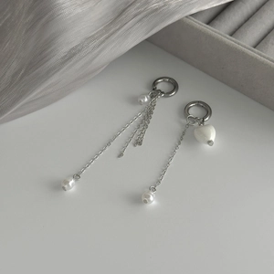 Détail de boucles d'oreilles argentées asymétriques avec chaînes et perles en cœur