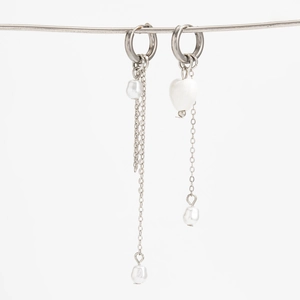 Détail de boucles d'oreilles asymétriques avec perles en cœur et chaînes argent
