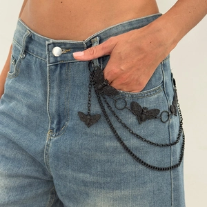 Détail de la chaîne de taille punk noire avec pendentifs papillon sur un jean bleu
