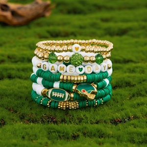Detail of stacked green and gold beaded bracelets with GAME DAY charms and football helmet