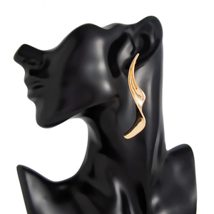 Primer plano de pendientes dorados estilo metal líquido sobre un busto de exhibición negro