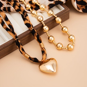 Detail of gold heart pendant with leopard print strap and bead chain on wood display