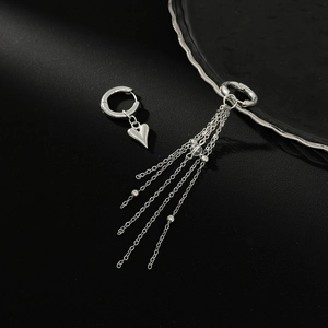 Détail de boucles d'oreilles argentées asymétriques avec cœur et pompons à chaîne