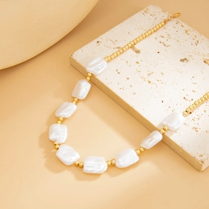 Detail of baroque pearl and gold bead necklace draped on a white textured stone