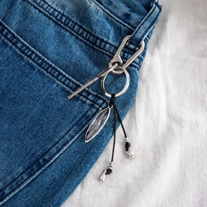 Detail of silver irregular acrylic gemstone pendant with metal keychain on denim jeans