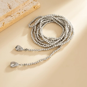 Detail van een zilveren kralenketting met vloeiende metalen harthangers op een steen