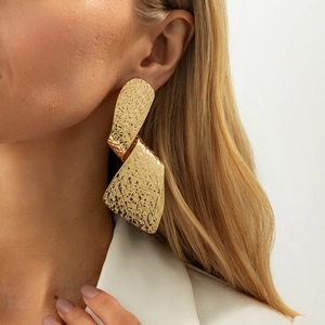 Detalle de pendientes geométricos dorados grandes con textura trenzada puestos en modelo