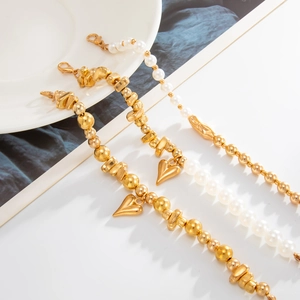 Detailansicht goldener Herzanhänger-Armbänder mit weißen Perlen und Metallperlen