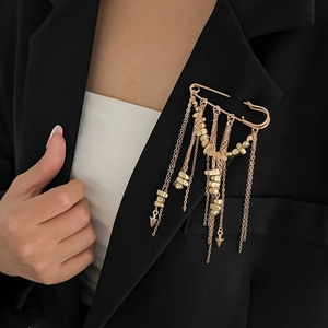 Détail d'une broche dorée à pompons et breloques sur le revers d'un tailleur noir