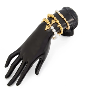 Detail von mehrlagigen Armbändern mit goldenen Herzanhängern und Perlen auf Handmodell