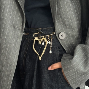 Detailed shot of golden lava heart brooch with pearl tassels pinned on denim waist