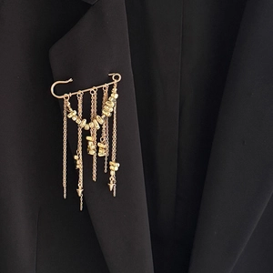 Détail d'une broche à pampilles dorées avec chaînes CCB sur le revers d'un blazer noir