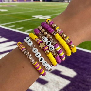 Detail of LSU Tigers themed purple and yellow beaded stack bracelets on a football field