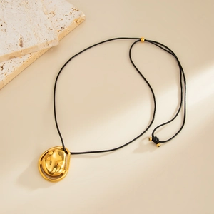 Detalle de colgante dorado irregular con cordón negro ajustable sobre fondo de piedra