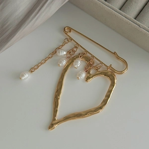 Macro detail of gold lava heart brooch featuring irregular metal texture and pearls