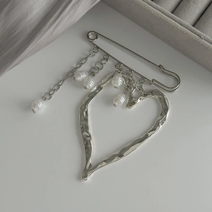 Detail of silver heart brooch with pearl tassel chain on elegant silk fabric background