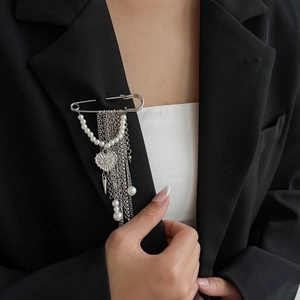 Détail d'une broche à franges argentées avec perles et pendentif cœur sur revers noir