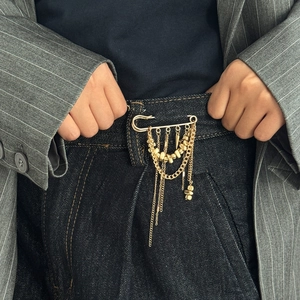 Détail d'une épingle à nourrice dorée à franges multicouches avec perles sur un jean