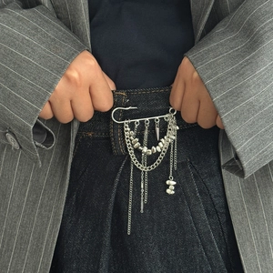 Détail de la broche à chaînes argentées superposées avec perles sur veste grise à rayures