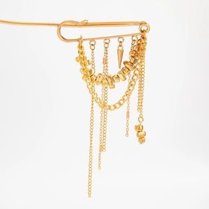 Dettaglio della spilla a nappe dorate con perle di metallo e catene multistrato punk