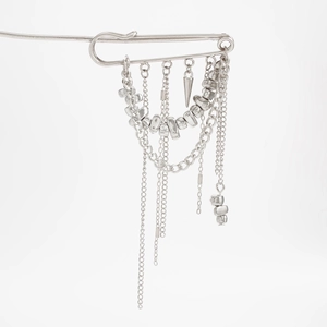 Détail d'une broche épingle à nourrice argentée avec chaînes à pompons et breloques punk