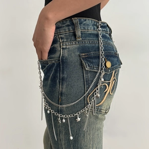 Detail van de gelaagde metalen tailleketting met sterren en parels op een spijkerbroek