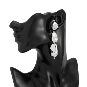 Détail de boucles d'oreilles en métal argenté irrégulier avec trois gouttes organiques