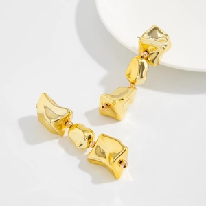 Détail macro de boucles d'oreilles pendantes dorées en métal liquide irrégulier