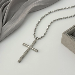 Close-up of vintage metal cross pendant and bead chain on elegant silk background