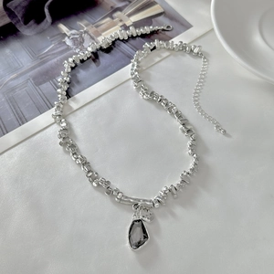 Detail of silver beaded necklace with grey water-drop gem pendant on silk background