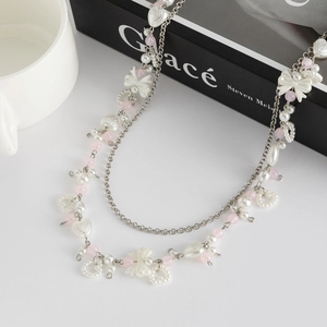 Detail van dubbele zilveren ketting met roze kralen, parels en hartvormige hangers