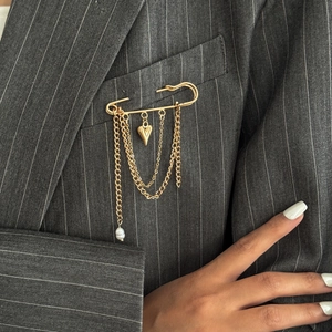 Dettaglio della spilla a cuore punk con catene dorate e perle su un blazer grigio