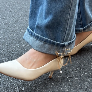 Dettaglio spilla dorata con catenelle di perle e pendenti su risvolto di jeans blu