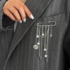 Detail of silver safety pin brooch with layered chains, stars, and pearls on grey suit