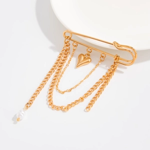 Close-up of golden safety pin brooch featuring hanging chains, heart charms and a white pearl