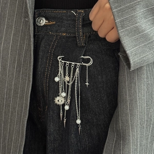 Detail of silver safety pin brooch with devil eye and pearls on denim jeans