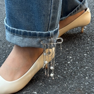 Detail of silver safety pin brooch with hanging pearls and star chain tassels on jeans